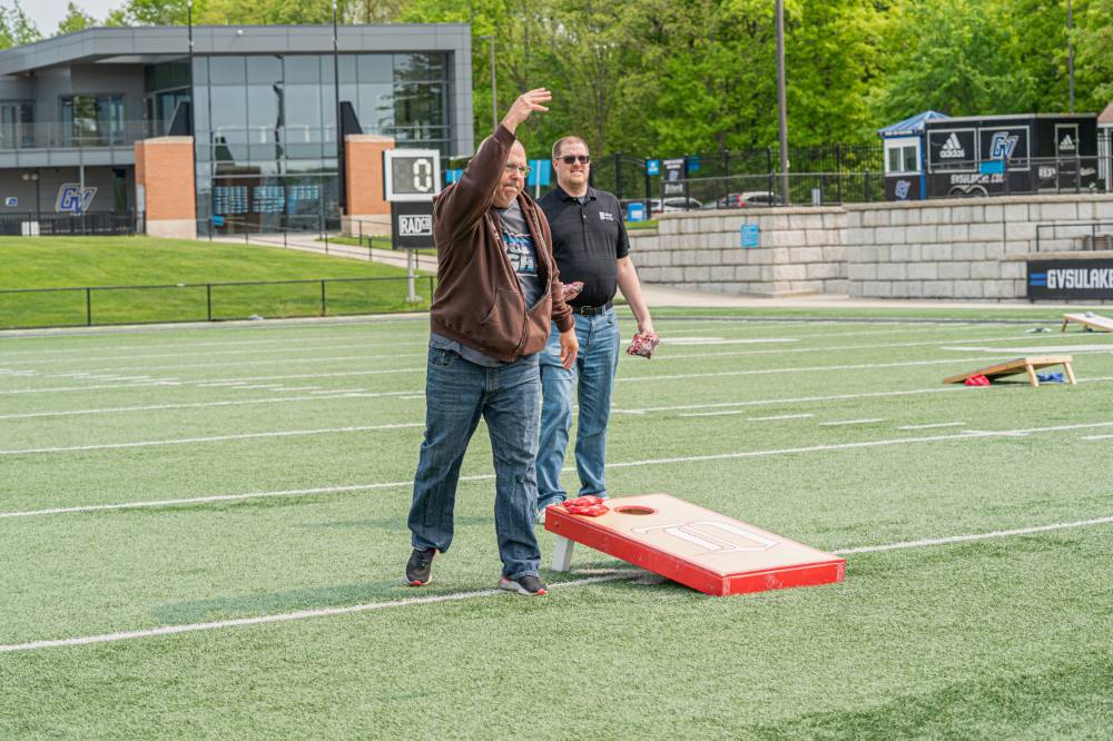 Man underhand tosses cornhole bag to the board opposite of him, as his opponent watches intently
